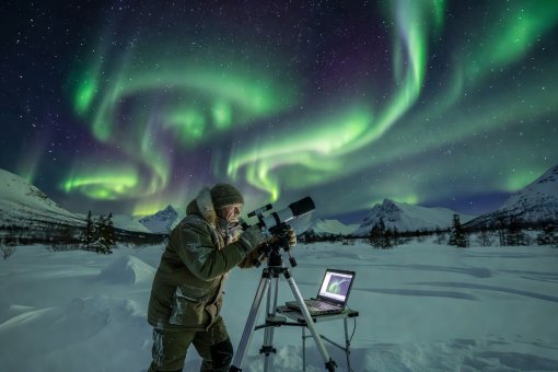 Scientific observer tracking auroral arcs against a dark starry sky above northern Norway