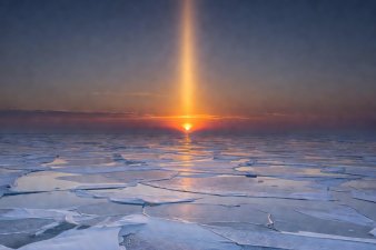 A striking vertical beam of amber light rising directly from a setting sun above frozen plains